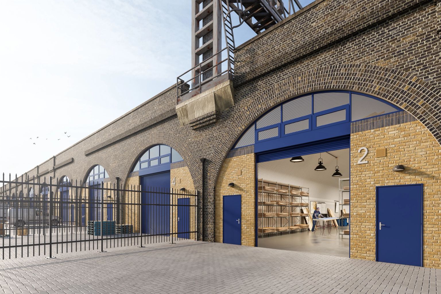 A long brick building of railway arches, with blue doors and an open archway revealing a modern office interior.
