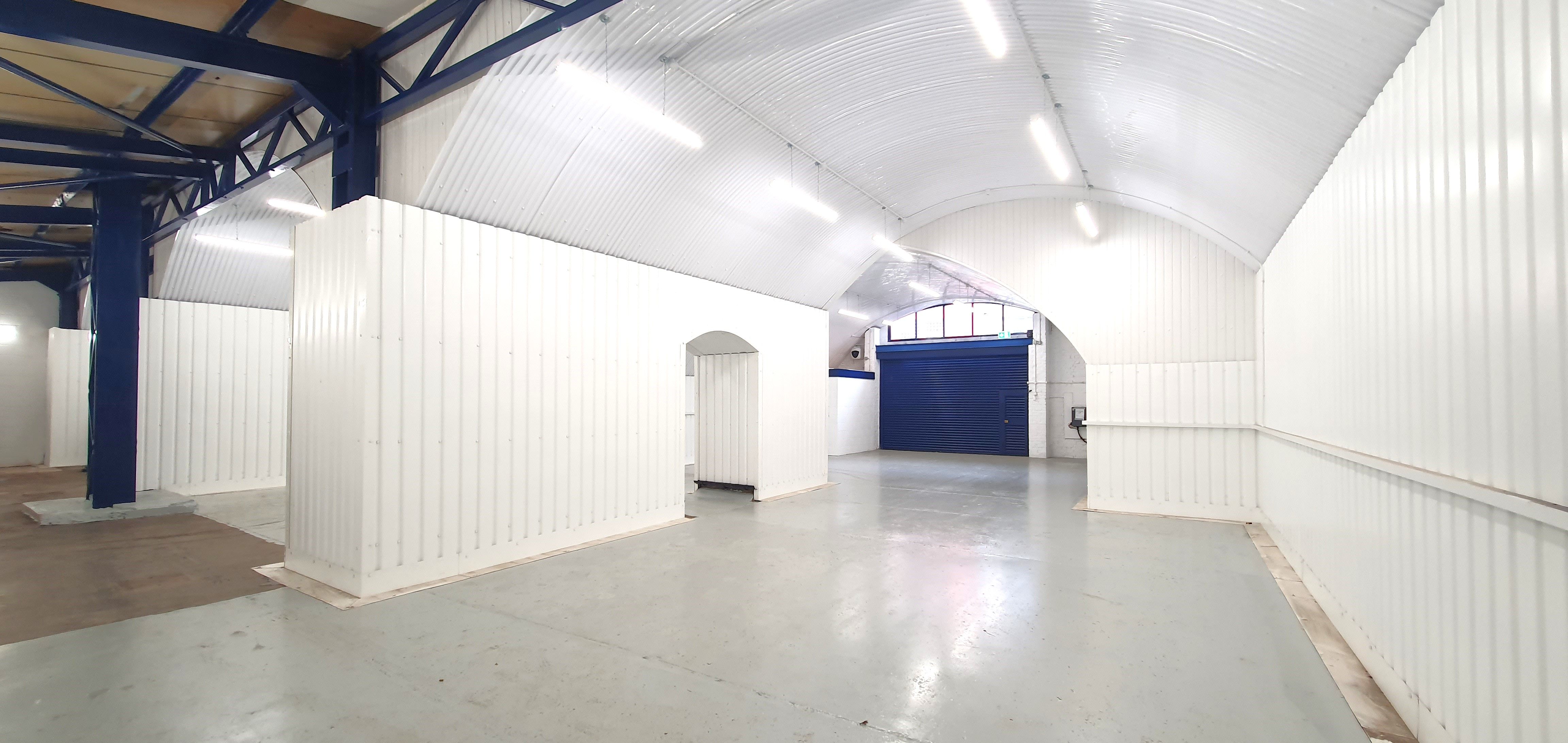 Empty self-storage facility with white corrugated units, an arched ceiling, and a blue roller door.