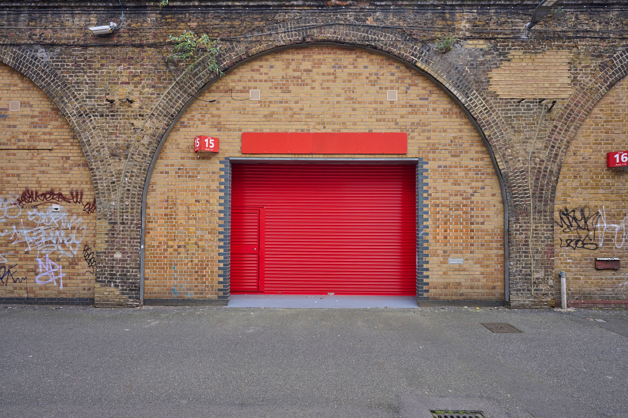 A bright red roll-down door centered in a brick archway, flanked by brick walls with graffiti.