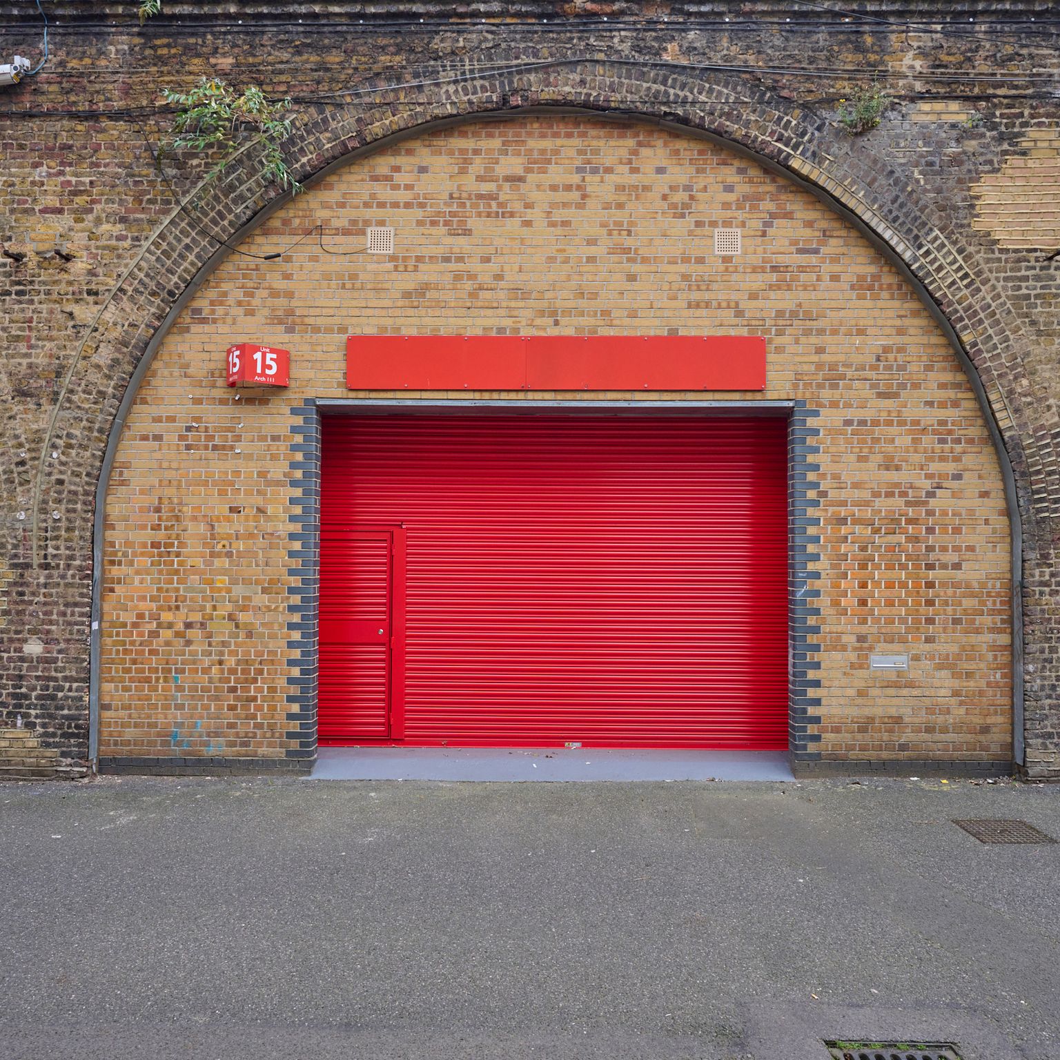 A bright red roll-down door centered in a brick archway, flanked by brick walls with graffiti.