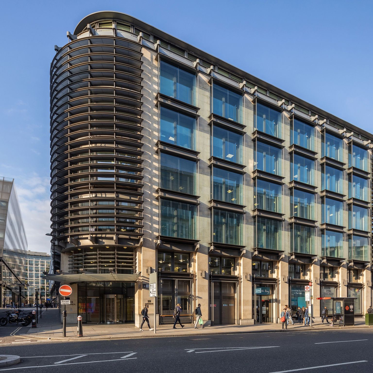 A modern building with a curved glass facade and horizontal louvers on a city street.