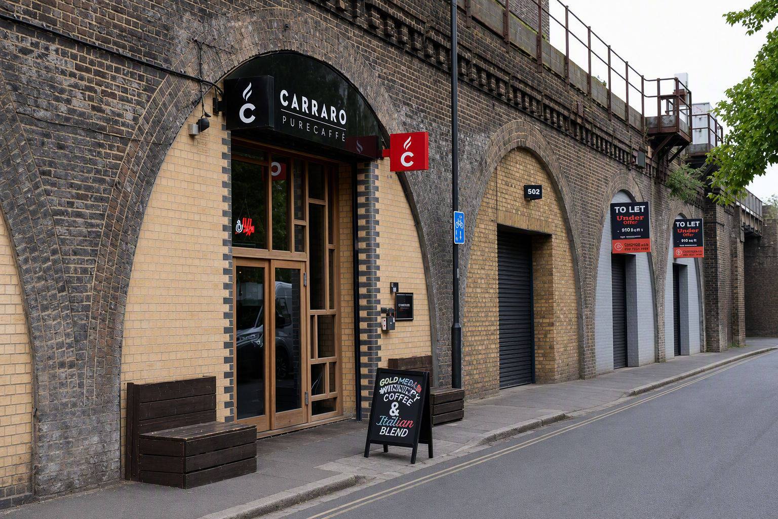 A row of shops, including "Beautiful Books," built into the brick arches of a railway viaduct alongside a street.