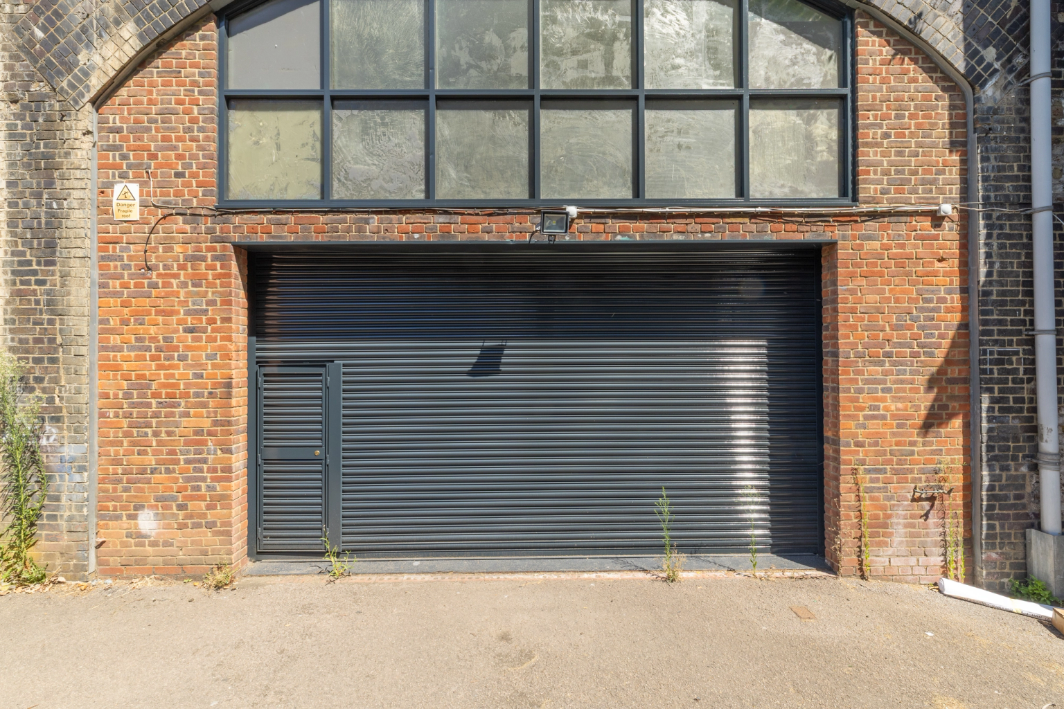 The front of an arch, with high level glazing, and a closed electric roller shutter entrance big enough for vehicle access.