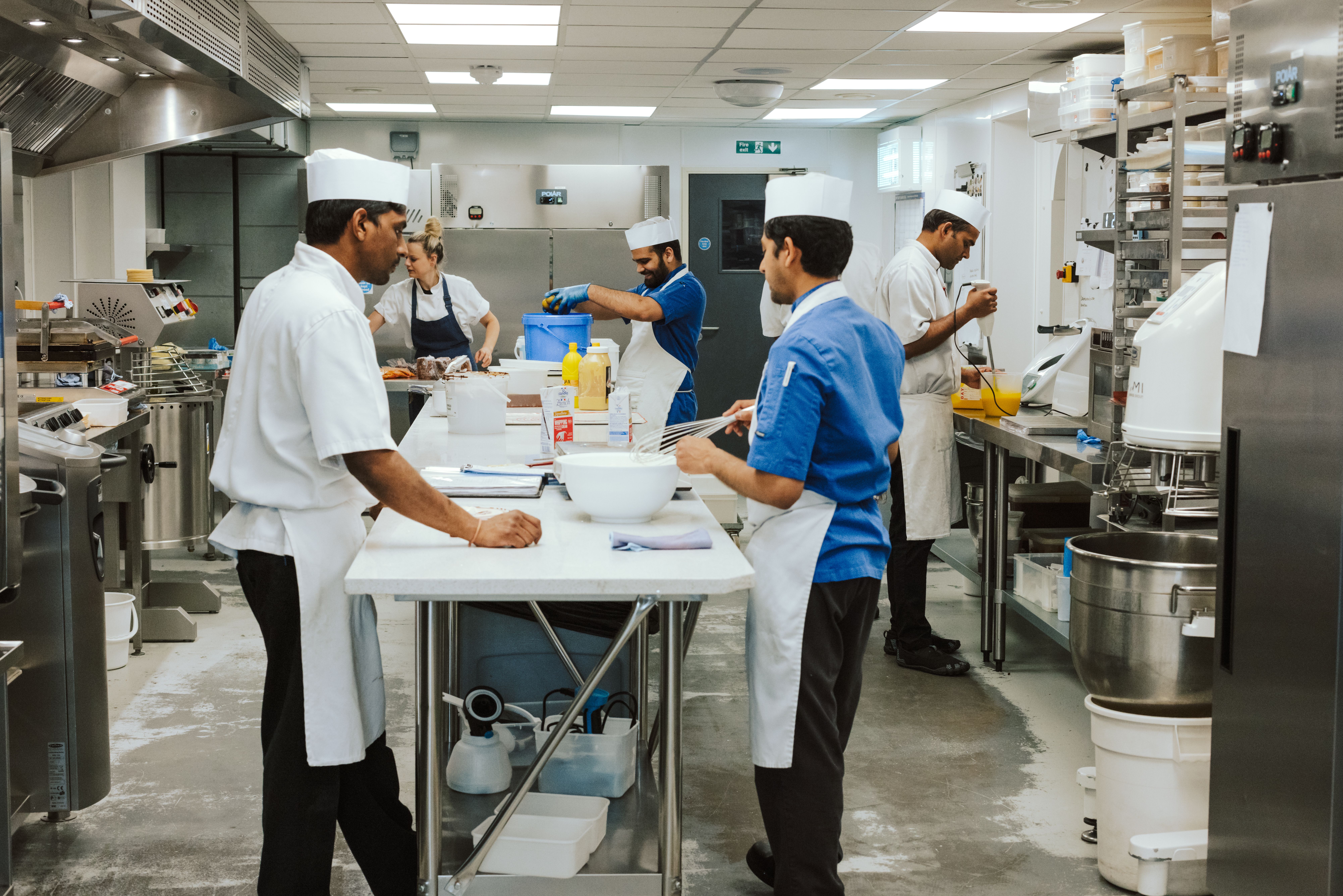 Chefs in white and blue uniforms prepare food in a professional kitchen.