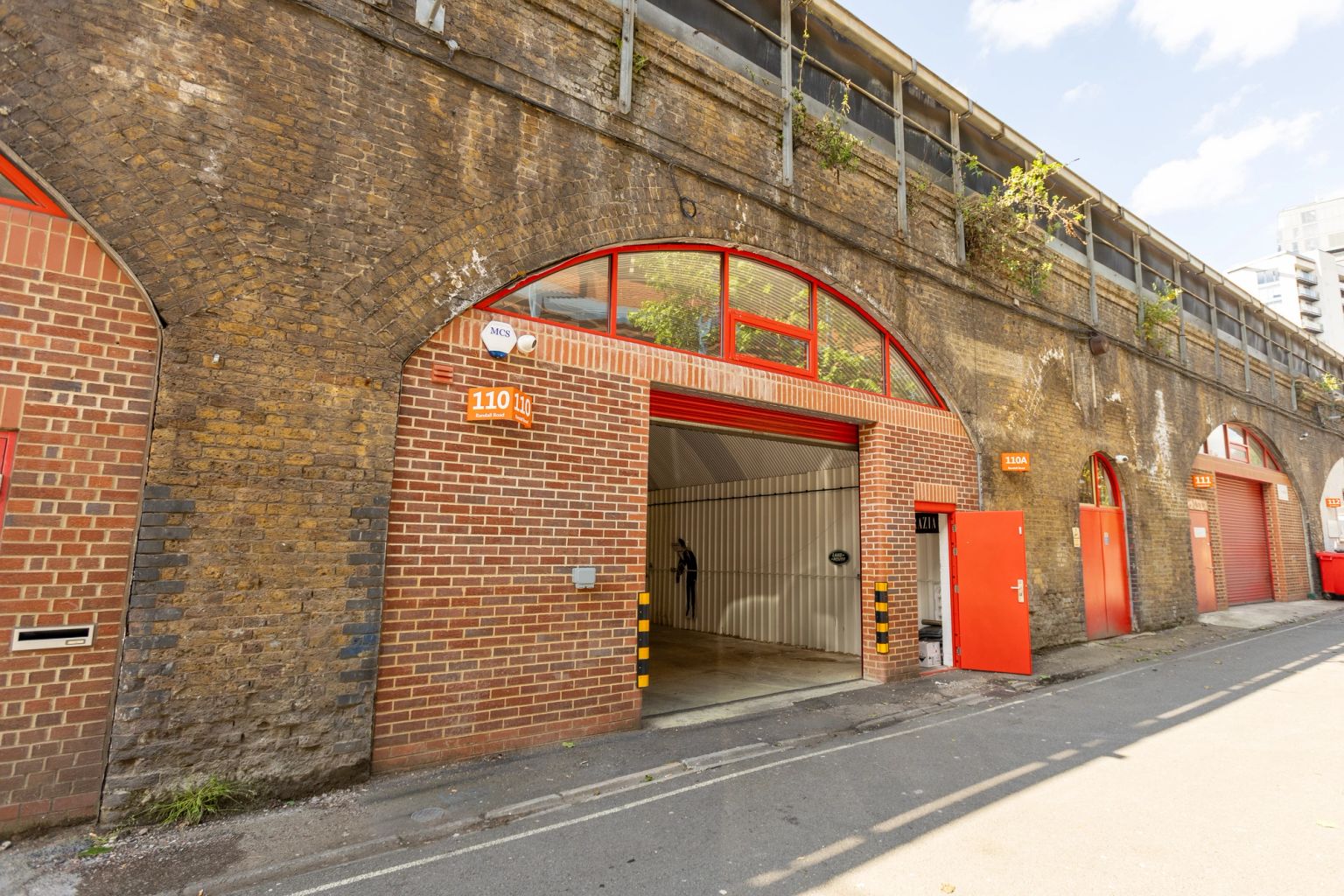 Row of brick railway arches with red doors, one arch open revealing an interior.