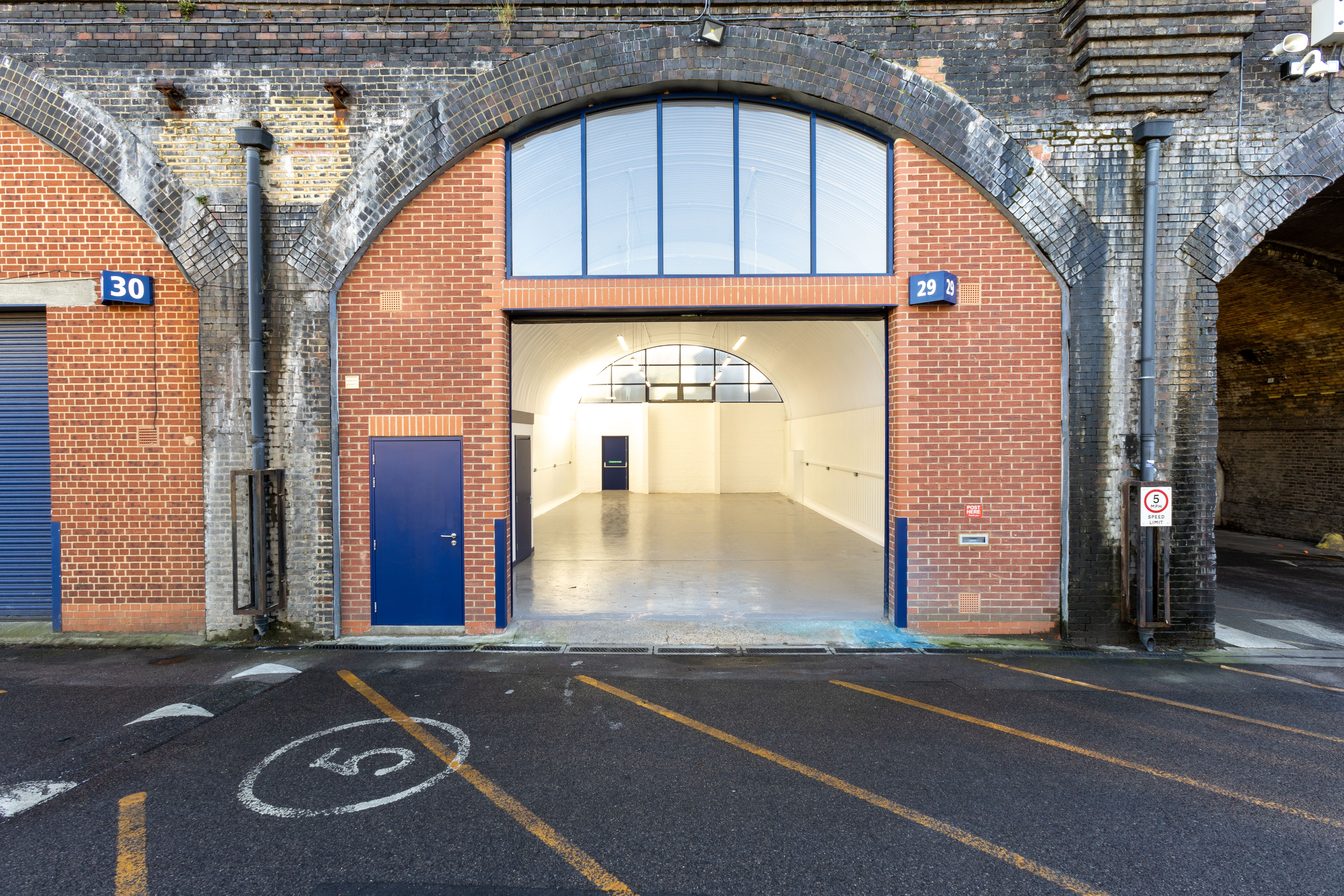 An empty, brightly lit industrial unit visible through an open brick railway arch (29), flanked by a blue-shuttered arch (30) and a dark tunnel arch.