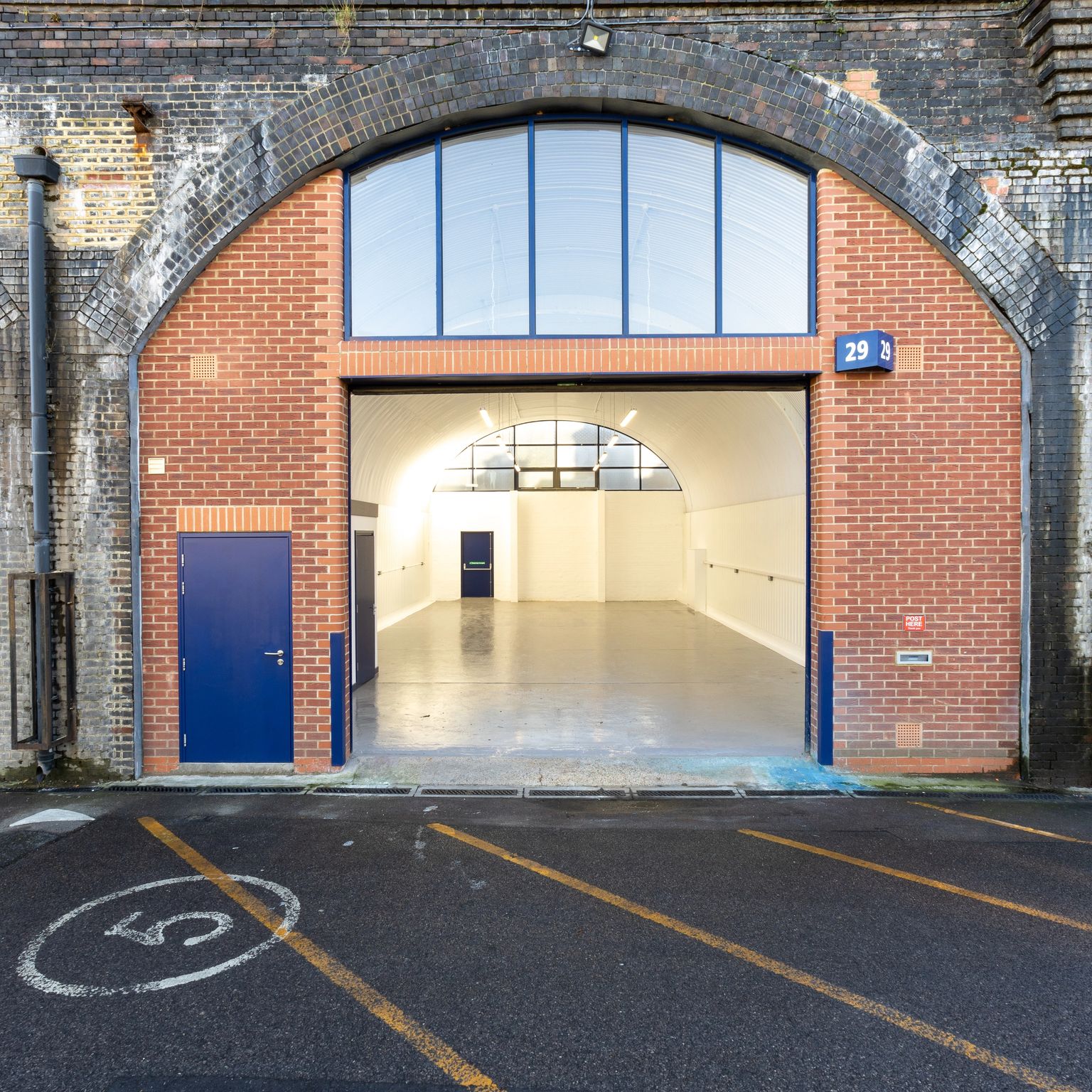 An empty, brightly lit industrial unit visible through an open brick railway arch (29), flanked by a blue-shuttered arch (30) and a dark tunnel arch.