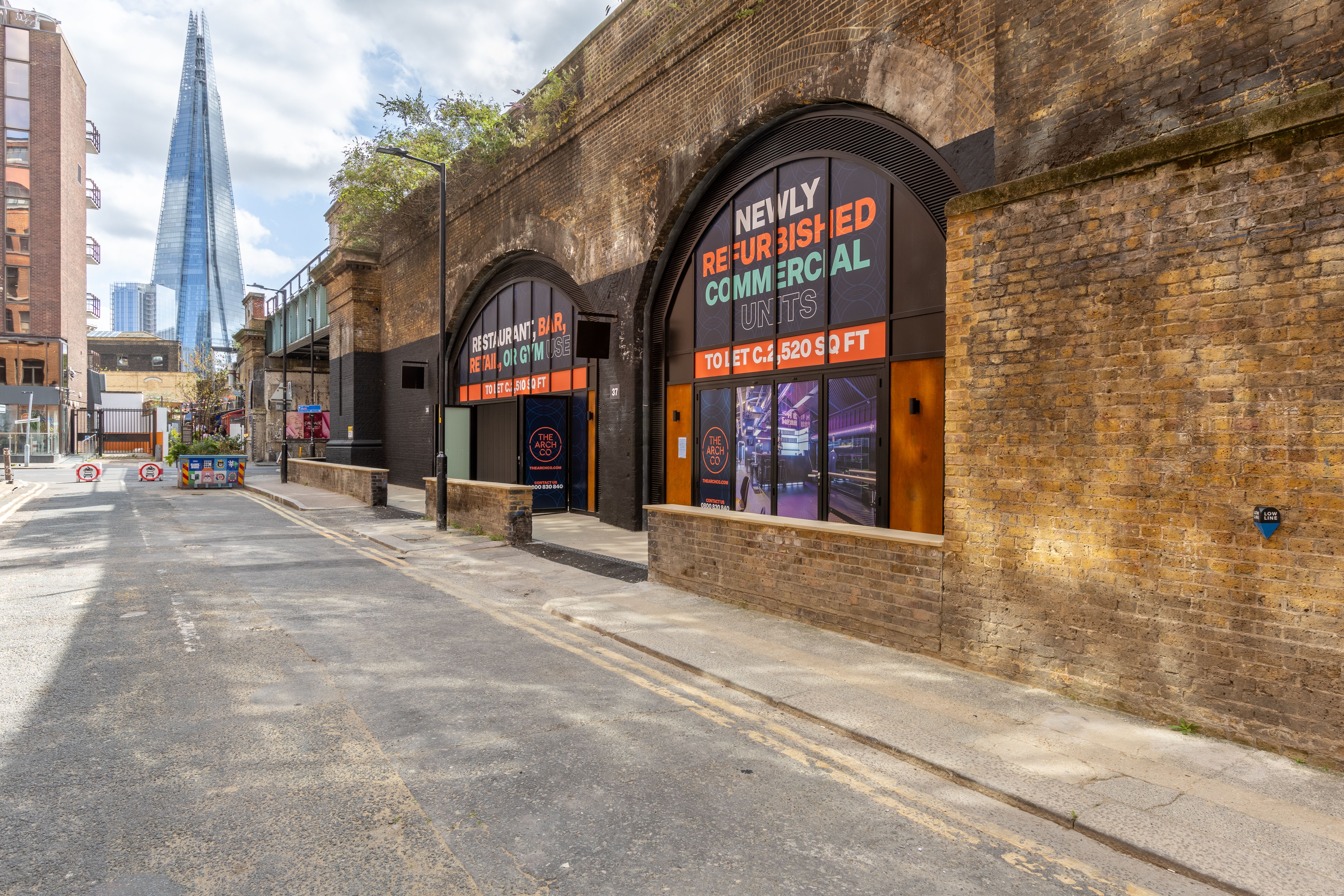 Quiet urban street with brick railway arches promoting commercial units, The Shard visible in the distance.