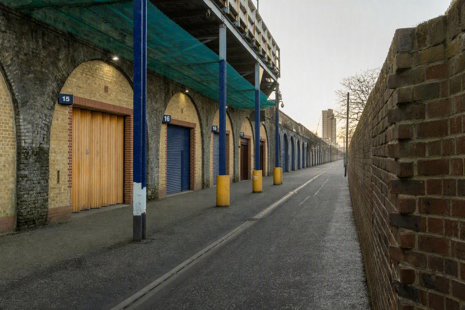 Modern glass-fronted businesses integrated into brick railway arches along an urban street with parked cars.