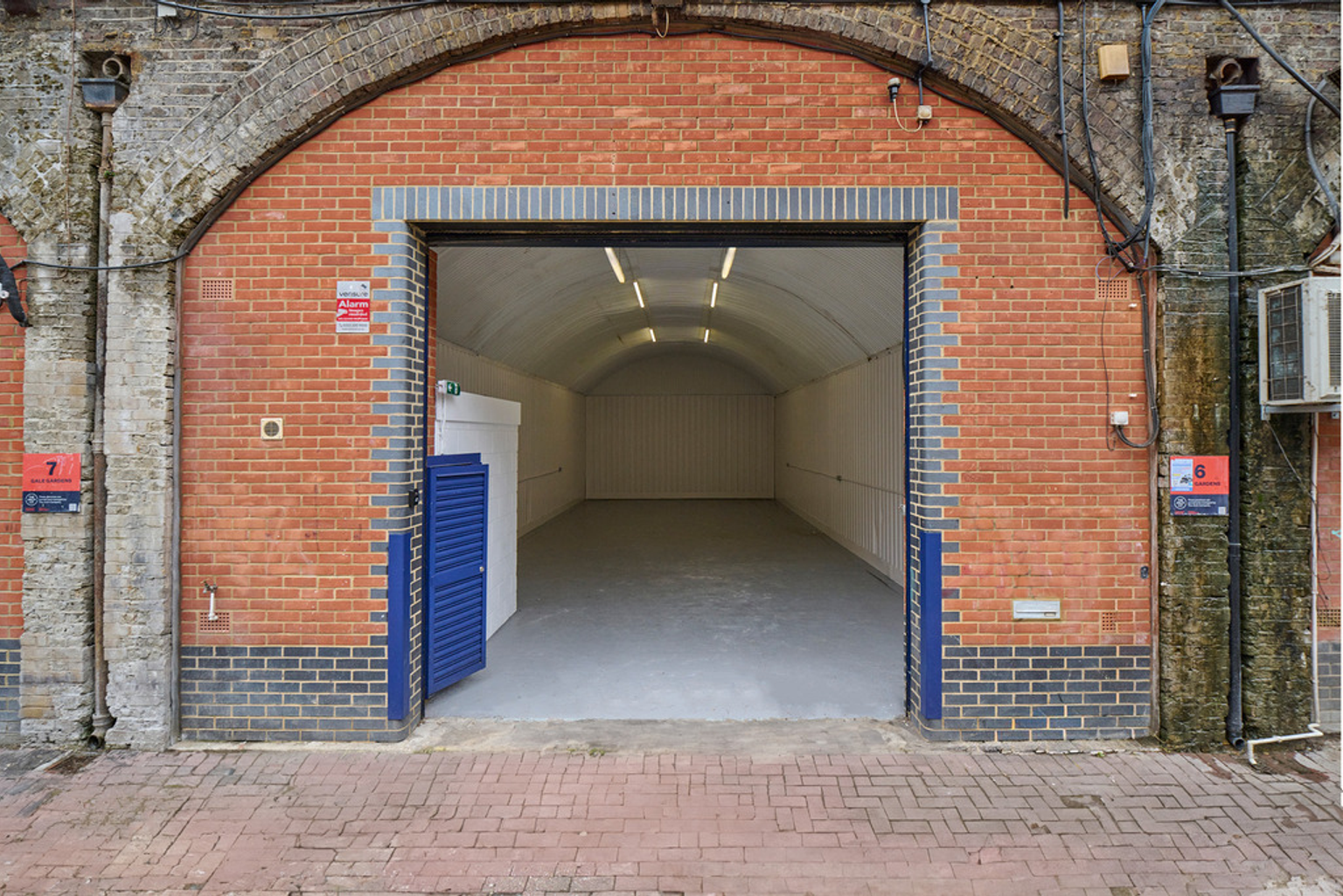 An empty arch with lining, facing the front electric roller shutter entrance, which is open.