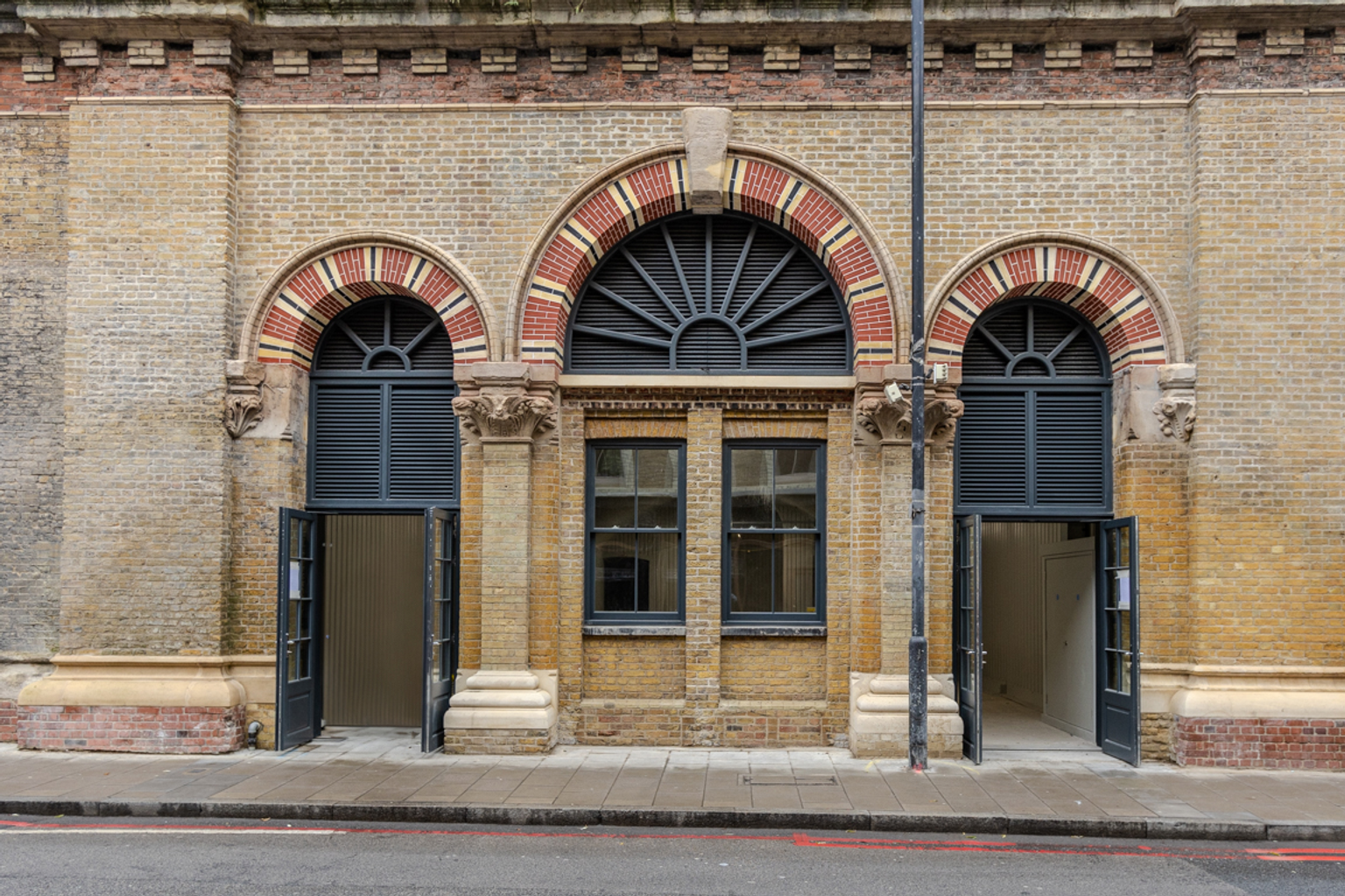 "London's Glitch" sign on a black-painted brick railway arch, with more arches visible to the right.