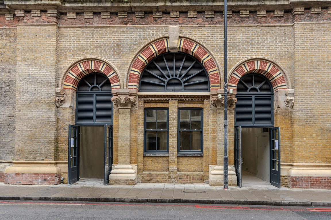 "London's Glitch" sign on a black-painted brick railway arch, with more arches visible to the right.
