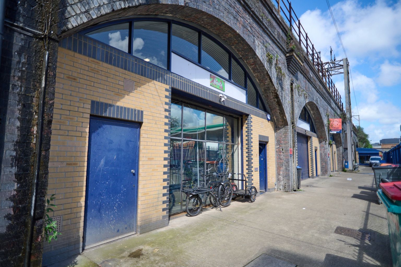 Row of shops, including a bike shop, in brick arches beneath a railway viaduct.