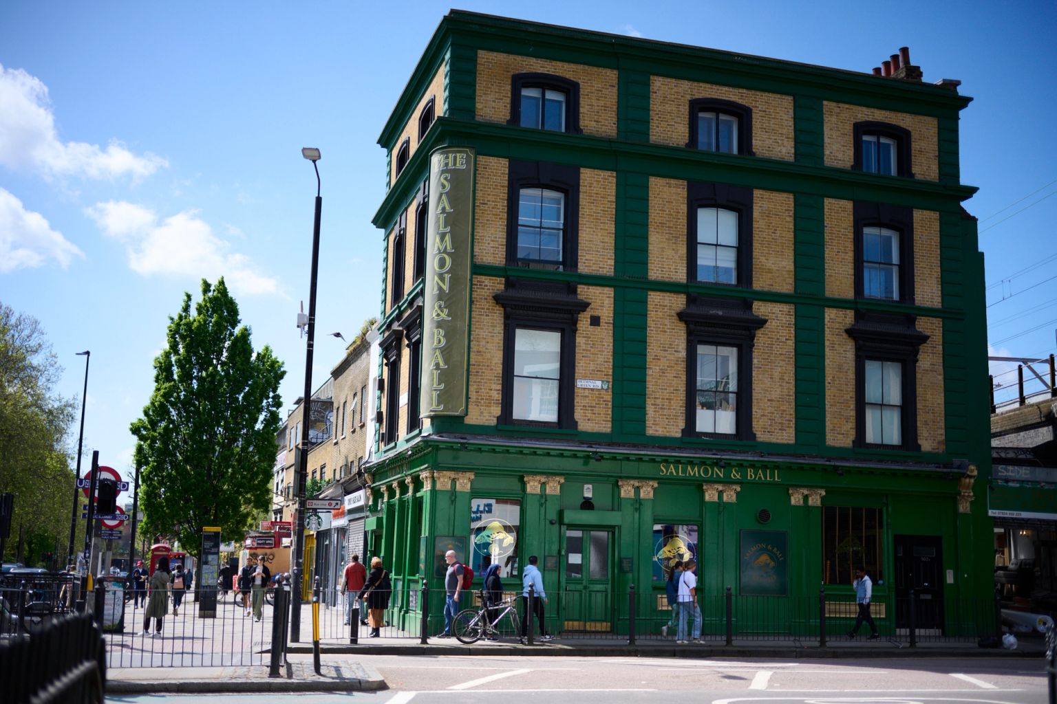 The Salmon & Ball pub, a green and yellow building, on an urban street corner with pedestrians.