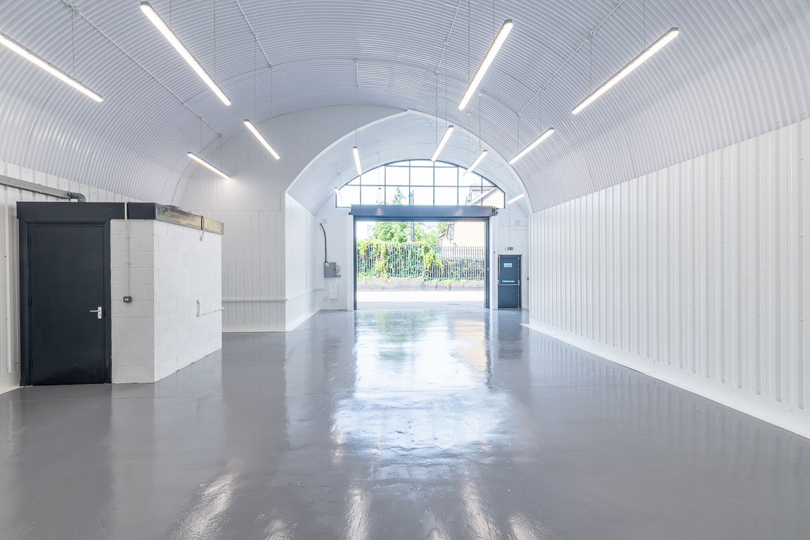 A modern, empty industrial space with white corrugated arched ceiling and walls, glossy grey floor, and an open doorway.