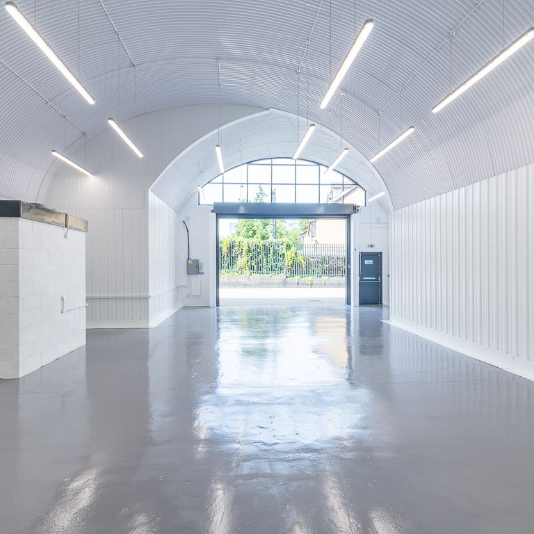 A modern, empty industrial space with white corrugated arched ceiling and walls, glossy grey floor, and an open doorway.