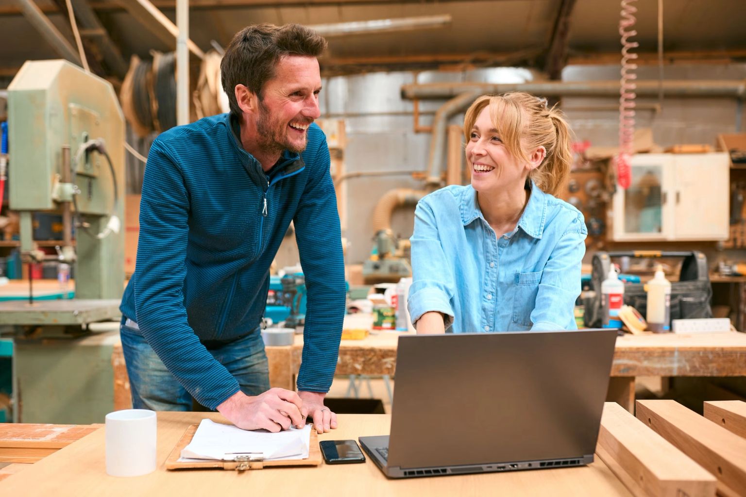 A happy man and woman working on a laptop in a workshop.