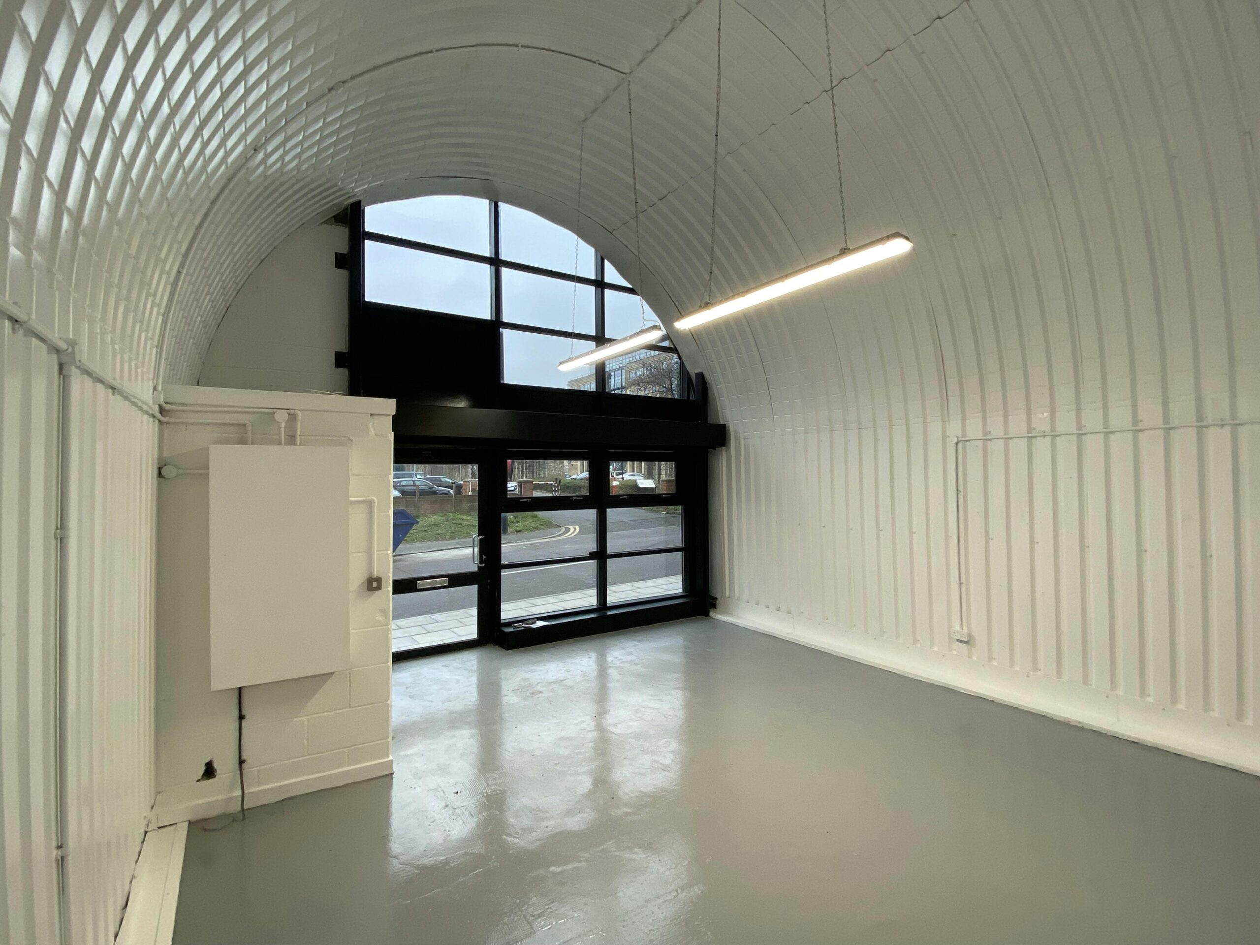 Interior of an empty, modern white industrial unit with an arched corrugated ceiling, gray floor, and large front windows.