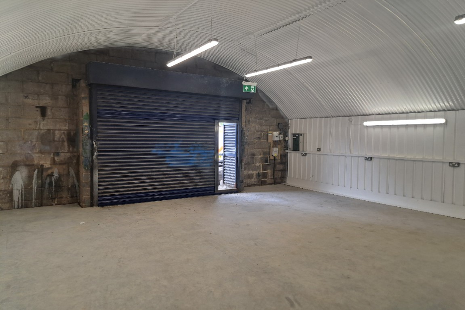 An empty arch with white lining, facing the front electric roller shutter entrance, which is open.