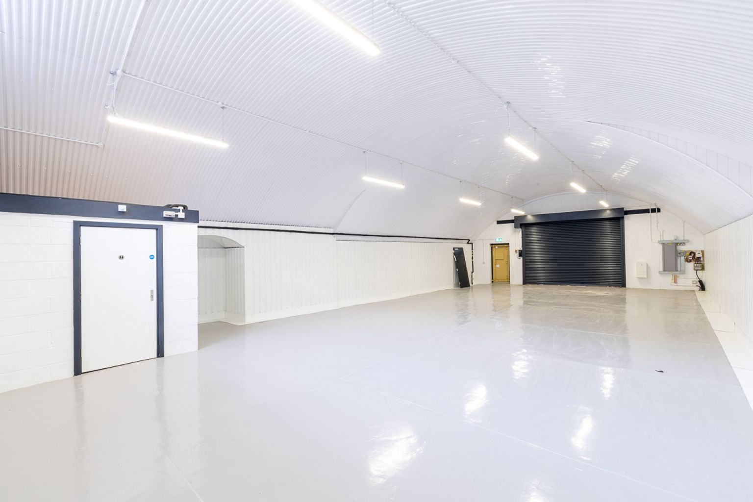 A bright, clean, empty white room with an arched, corrugated ceiling and various doors.