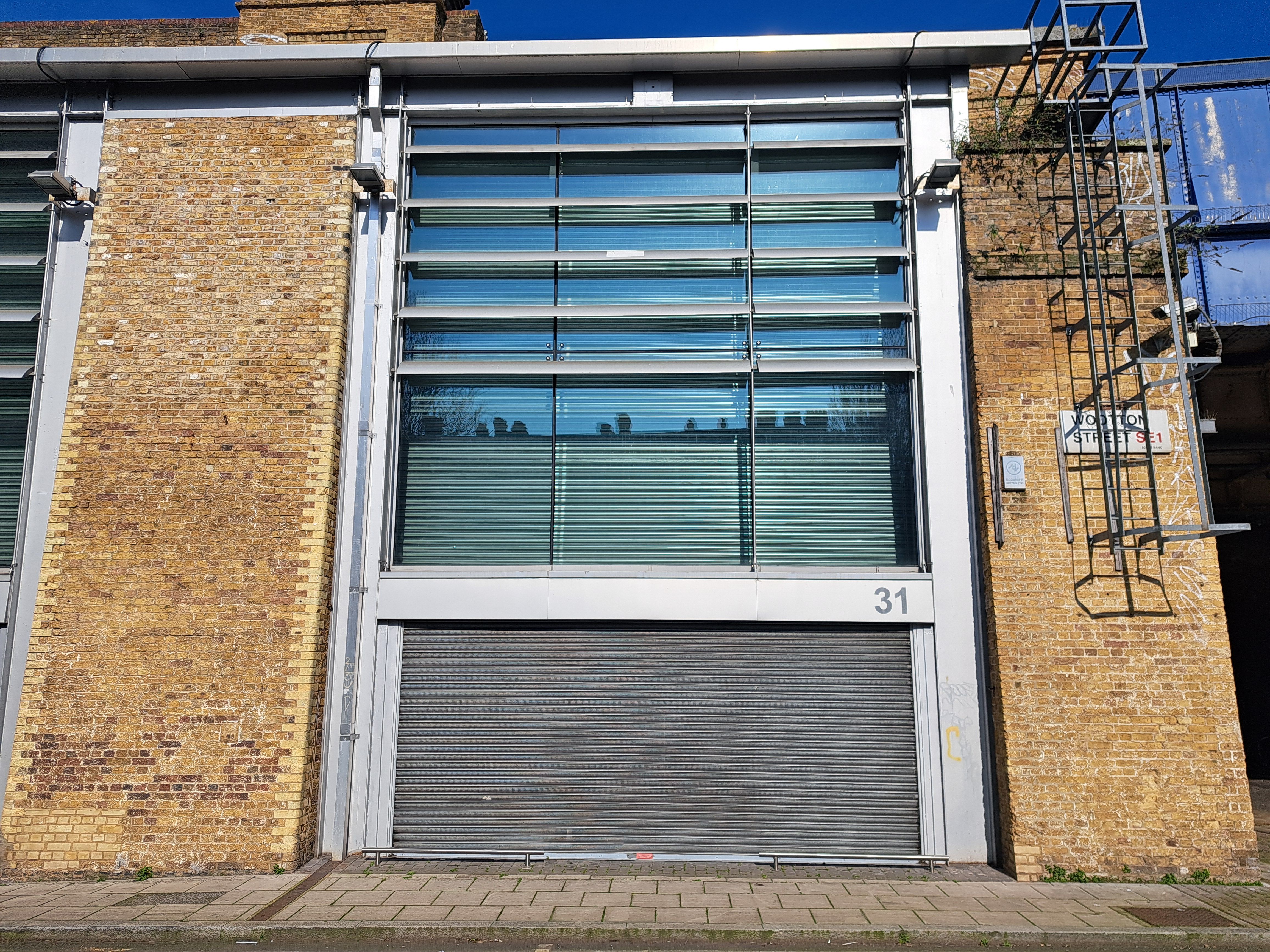 Building with brick walls, large glass windows, a roll-down garage door numbered 31, and an exterior metal ladder.
