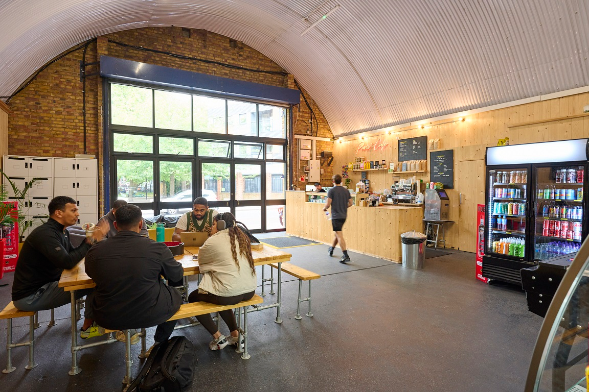 Cafe interior with a vaulted, corrugated metal ceiling, showing customers at a communal table and a service counter.