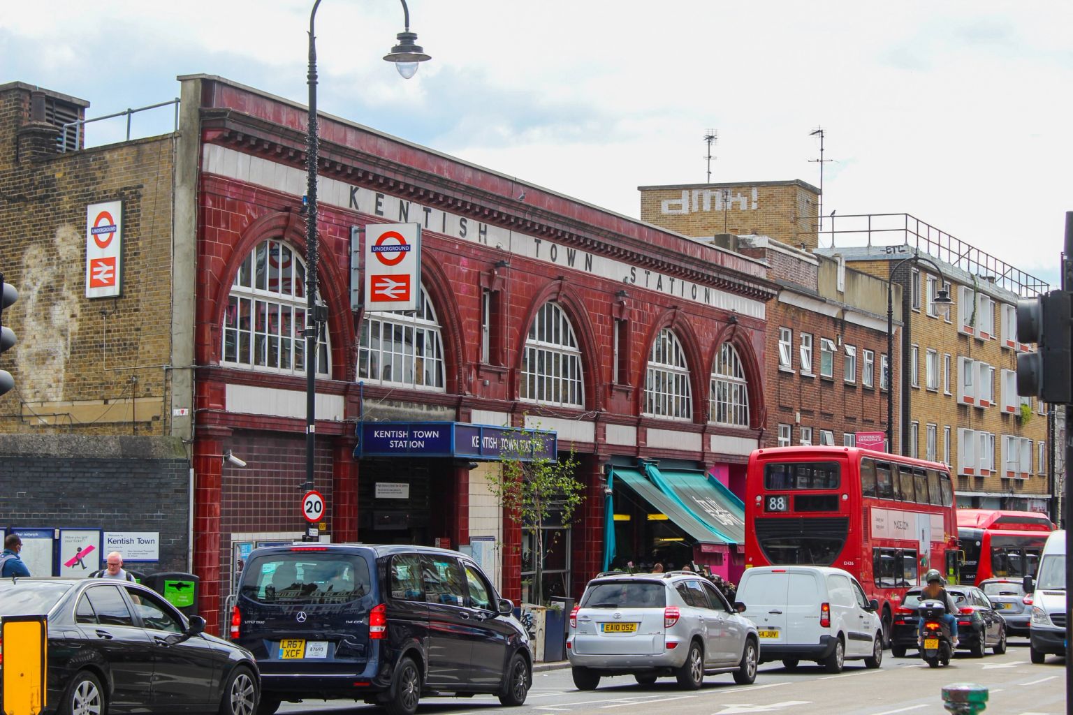 A street corner with a white and brick building, a parked black car, and a brick railway archway over the road.