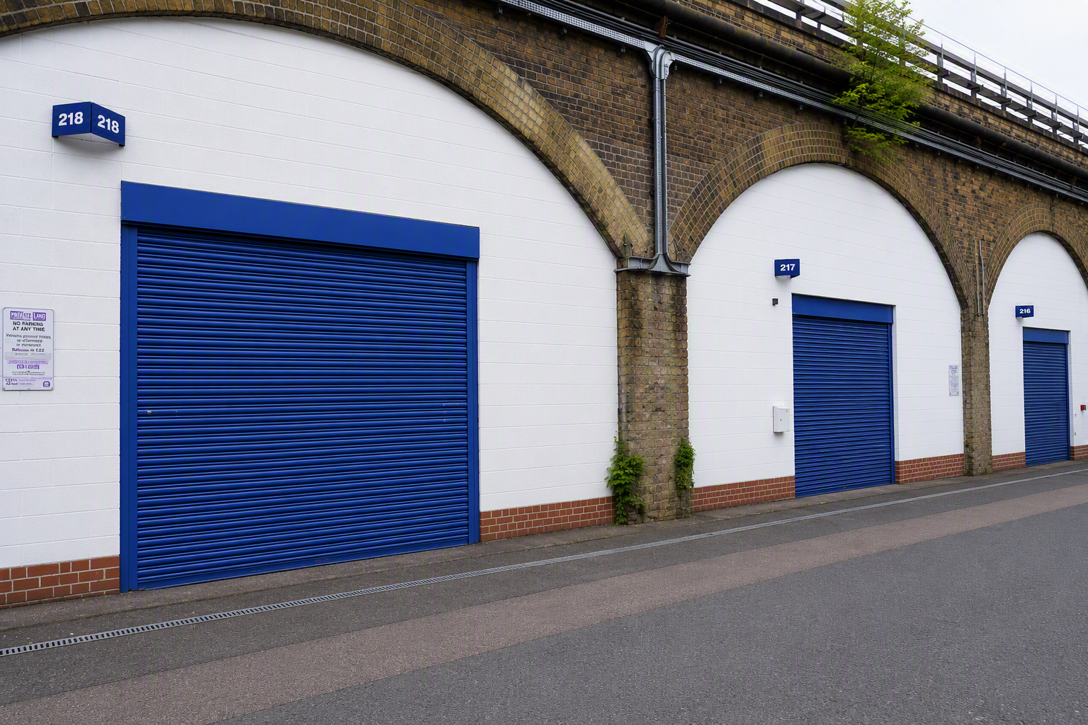 Modern glass-fronted businesses built into old brick railway arches, with cars parked on a street.