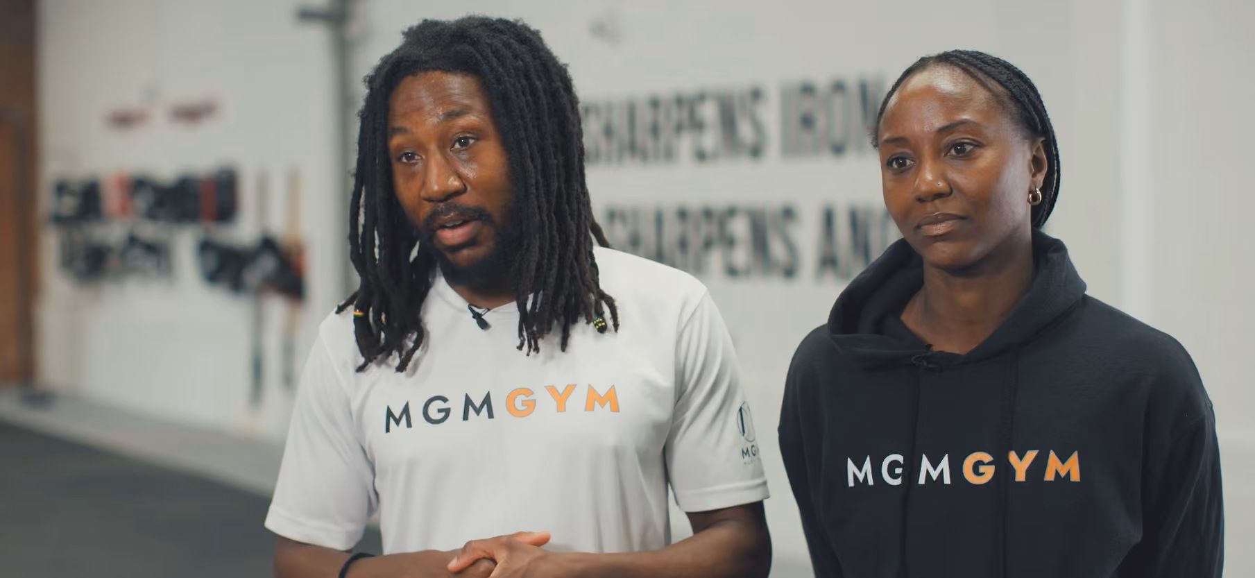 A man and woman wearing MGM GYM branded apparel stand in a gym.