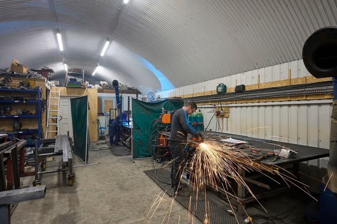 A person in a workshop grinds metal, producing a shower of bright sparks.