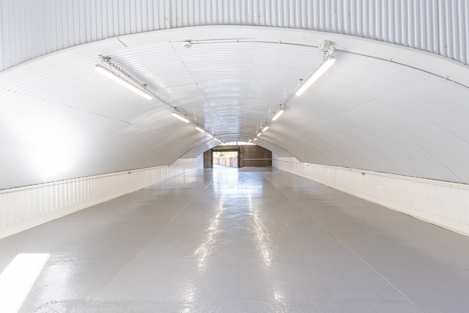 An empty arch with white lining, facing the front electric roller shutter entrance, which is closed.
