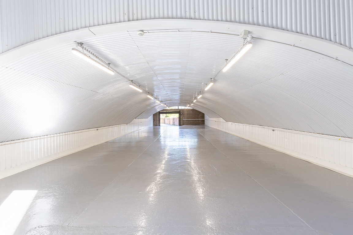 An empty arch with white lining, facing the front electric roller shutter entrance, which is closed.