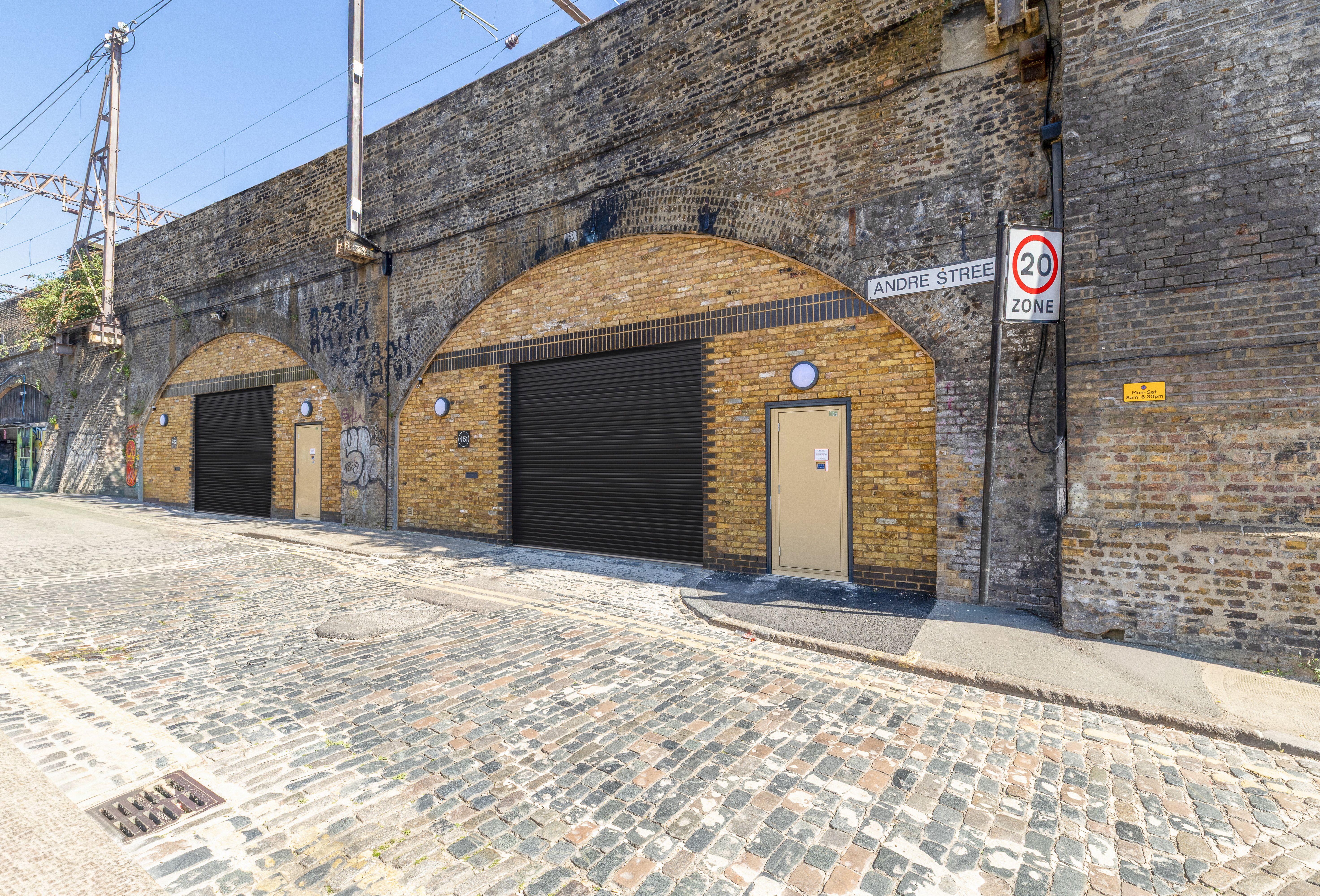 Two brick railway arches converted into units with black shutters and beige doors, seen from a cobbled street.