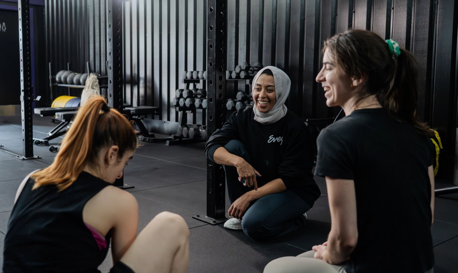 Three women smiling and talking in a gym.