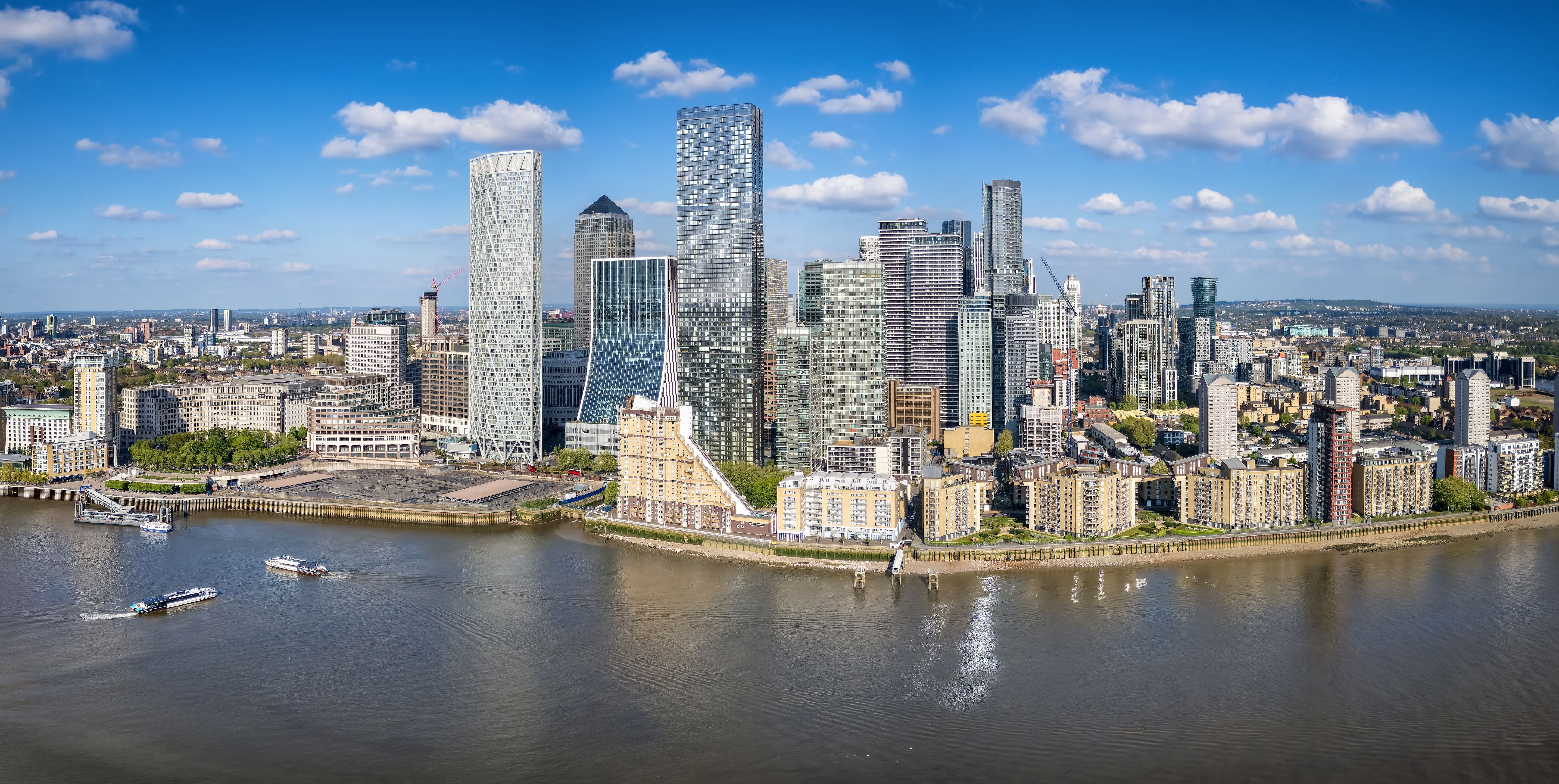 Aerial view of Canary Wharf's modern skyline along the River Thames with boats.