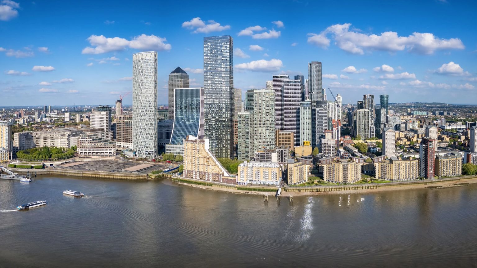 Aerial view of Canary Wharf's modern skyline along the River Thames with boats.