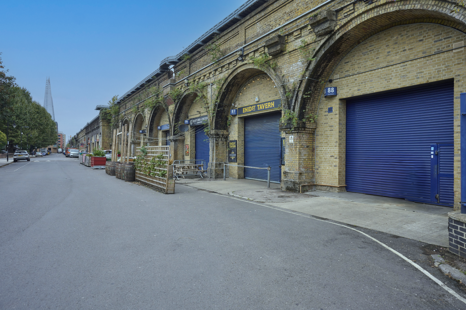 A street scene featuring arched railway viaducts repurposed for commercial use, with The Shard skyscraper visible in the background.