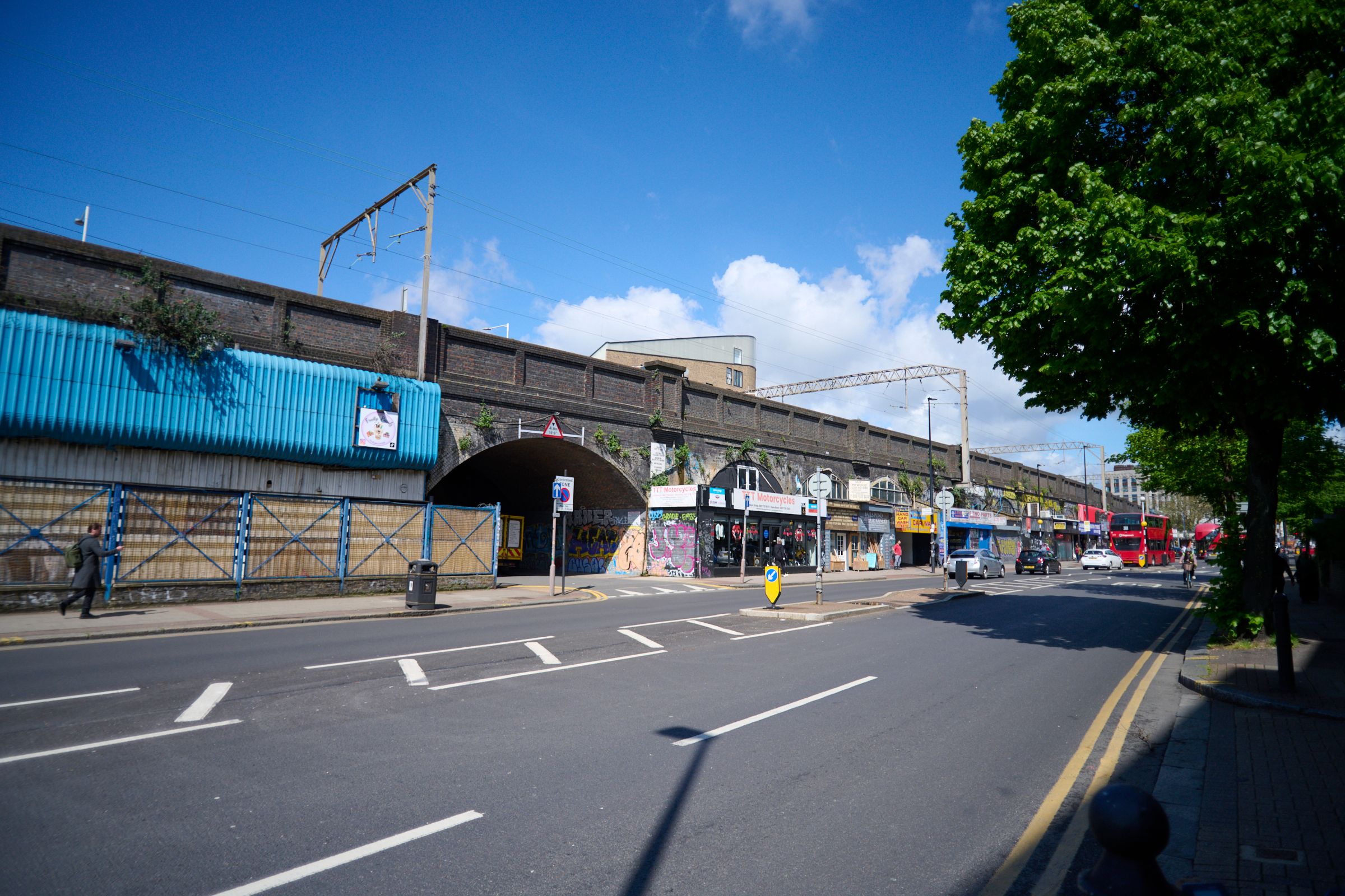 A man on a bicycle rides down an urban street with brick railway arches and a bike-themed planter.