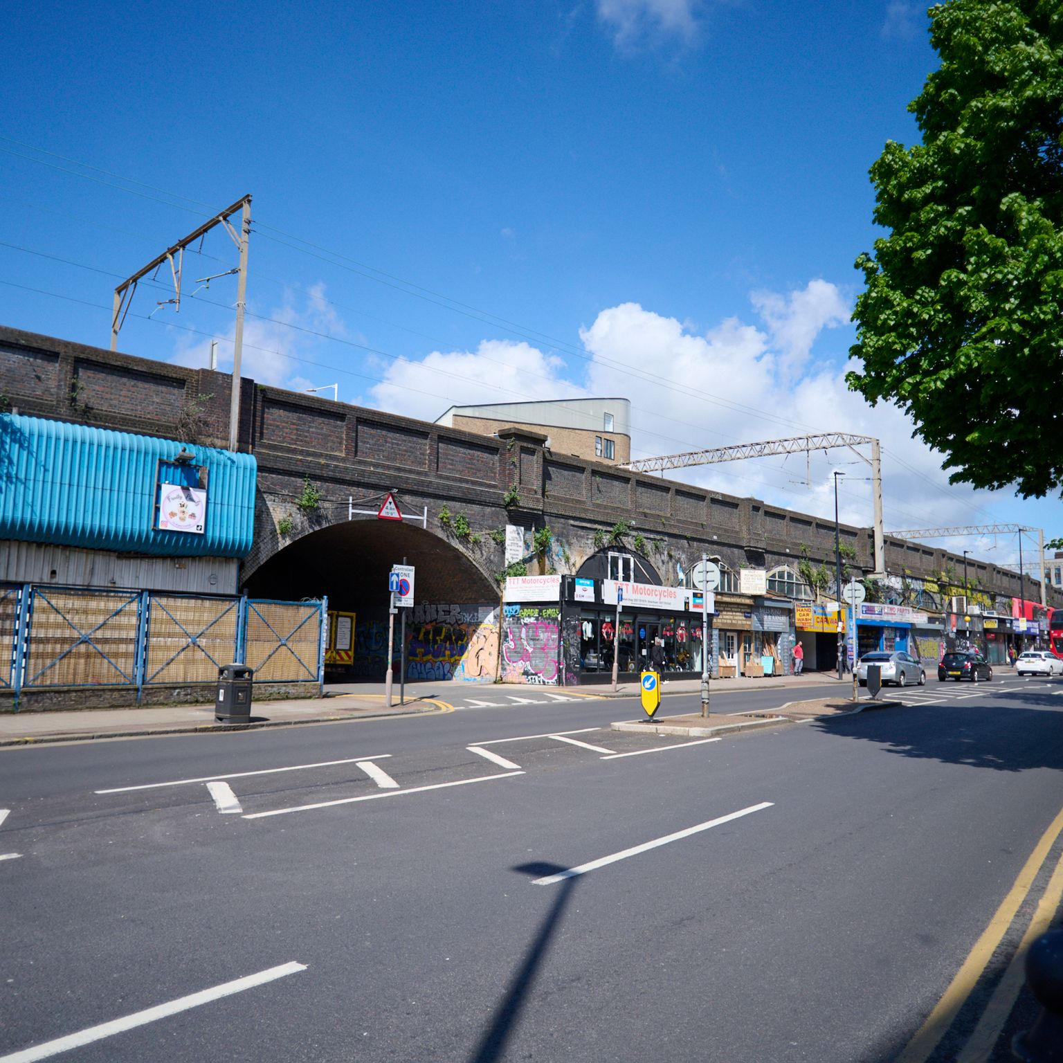 A man on a bicycle rides down an urban street with brick railway arches and a bike-themed planter.
