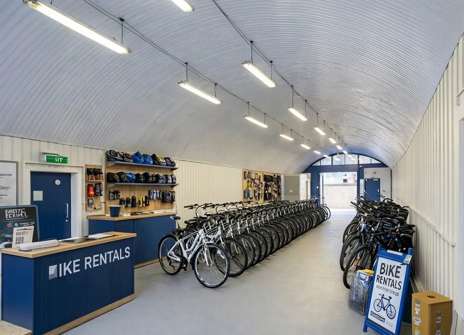 Interior of a bike rental facility with a vaulted ceiling, a reception counter, and many bicycles arranged in rows.