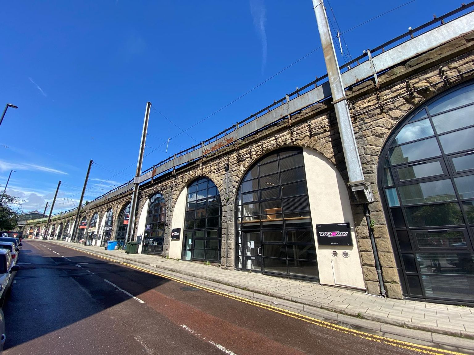 Row of stone railway arches converted into shops along a street under a blue sky.