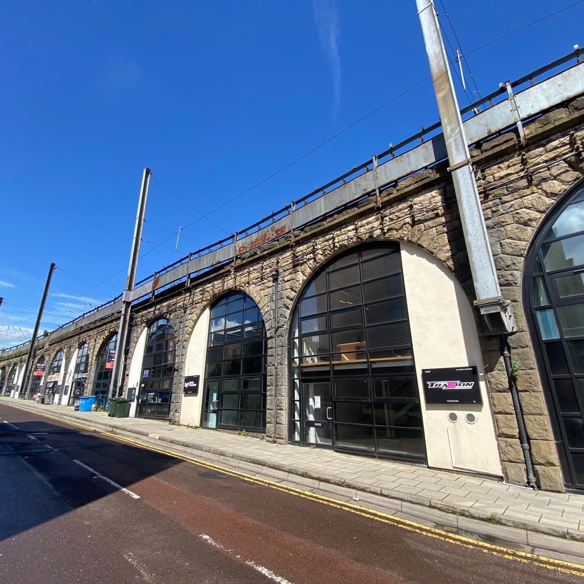 Row of stone railway arches converted into shops along a street under a blue sky.