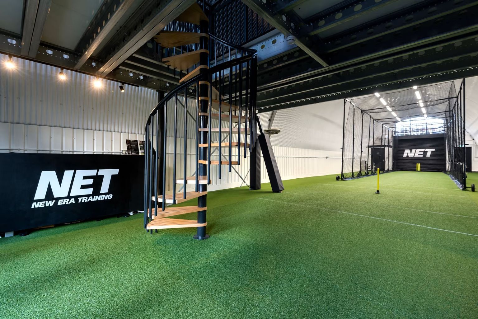 Indoor sports training facility with green turf, a black spiral staircase, and NET New Era Training branding.
