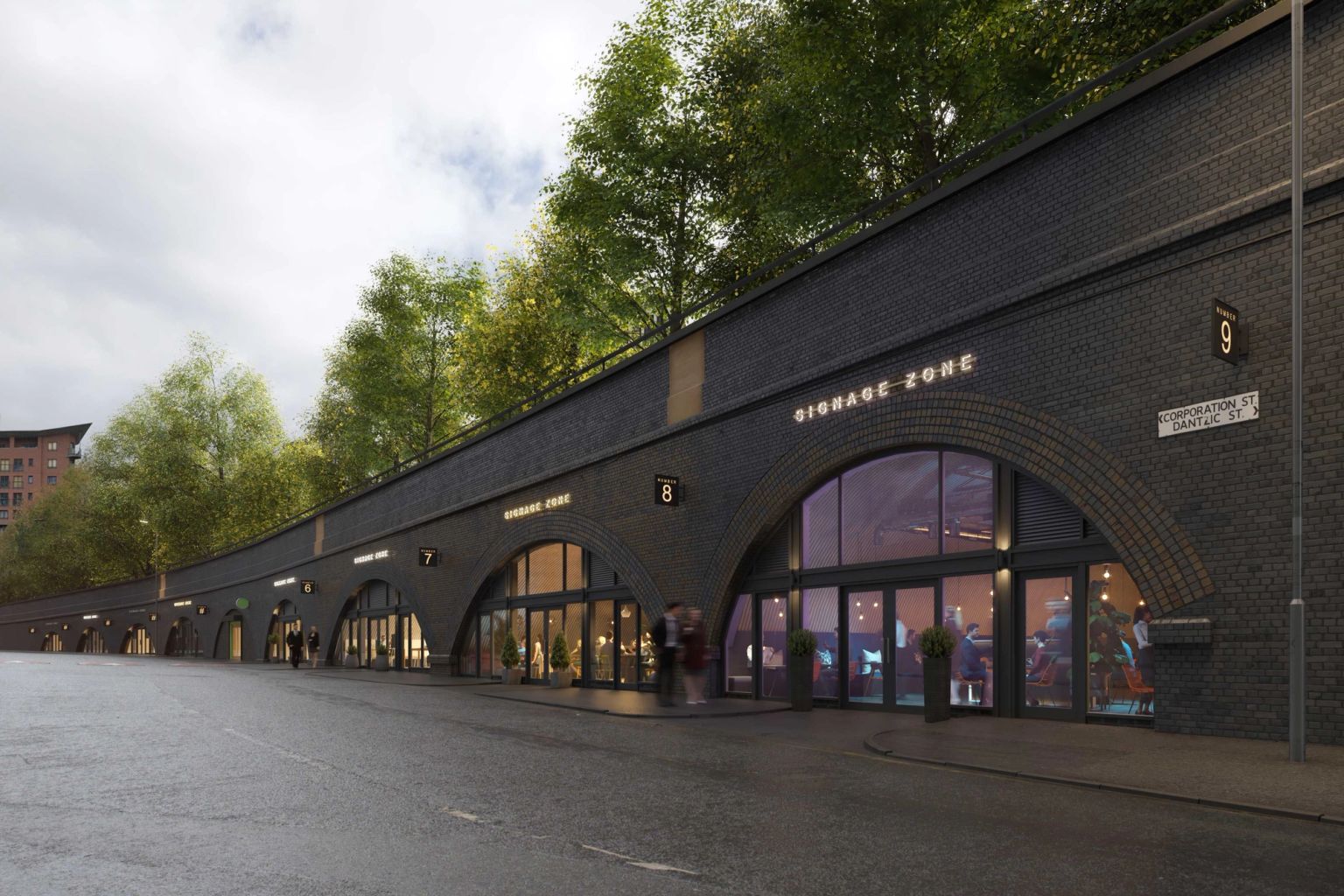 A long row of dark brick railway arches repurposed as modern shops with glass facades, beneath a tree-lined embankment.