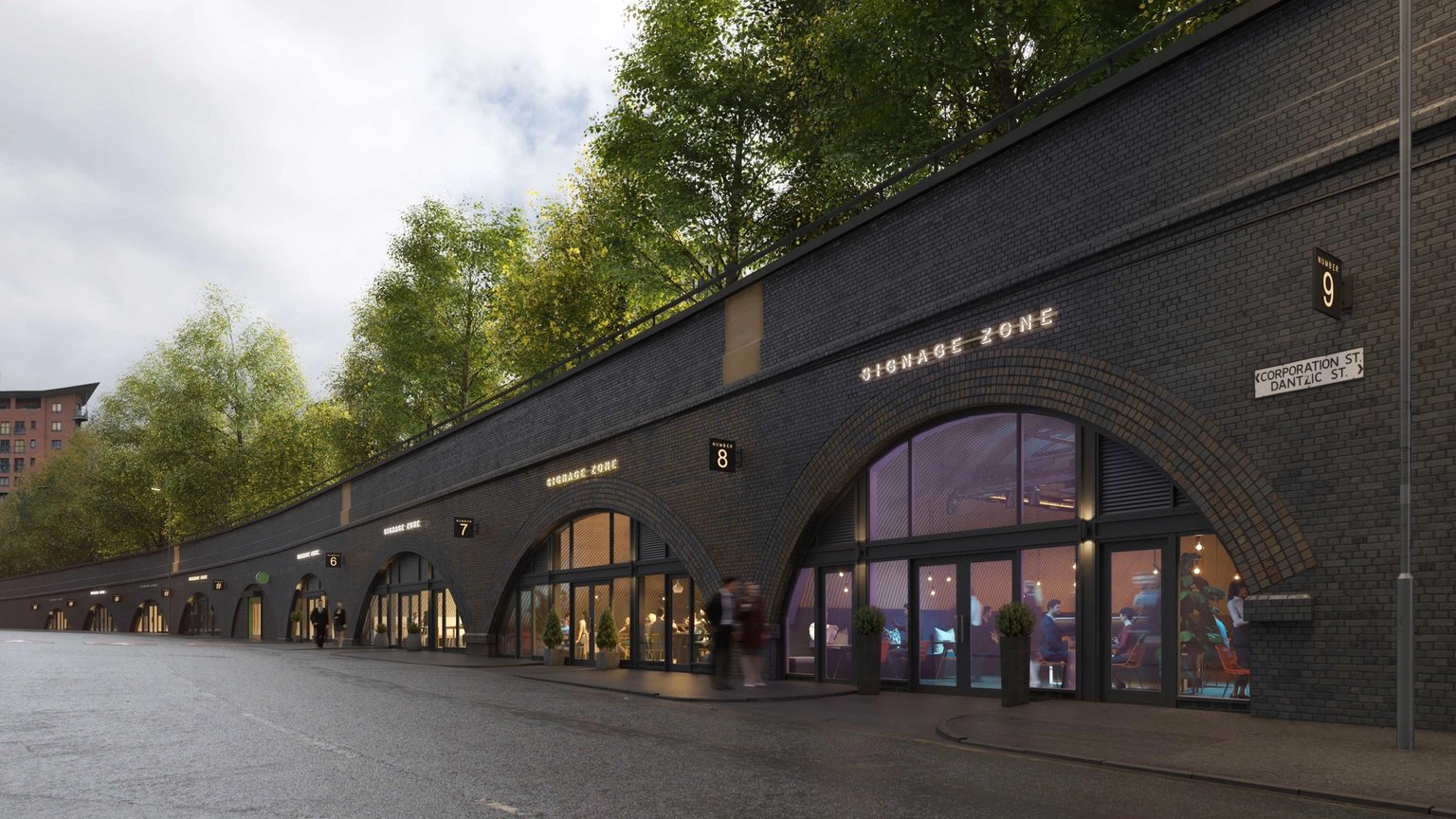 A long row of dark brick railway arches repurposed as modern shops with glass facades, beneath a tree-lined embankment.