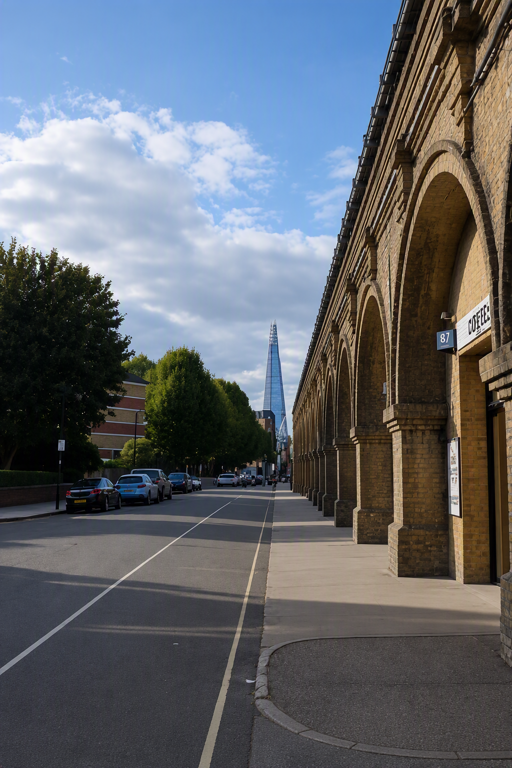 People dine outdoors at a cafe under brick arches, with The Shard visible in the distance on a sunny day.