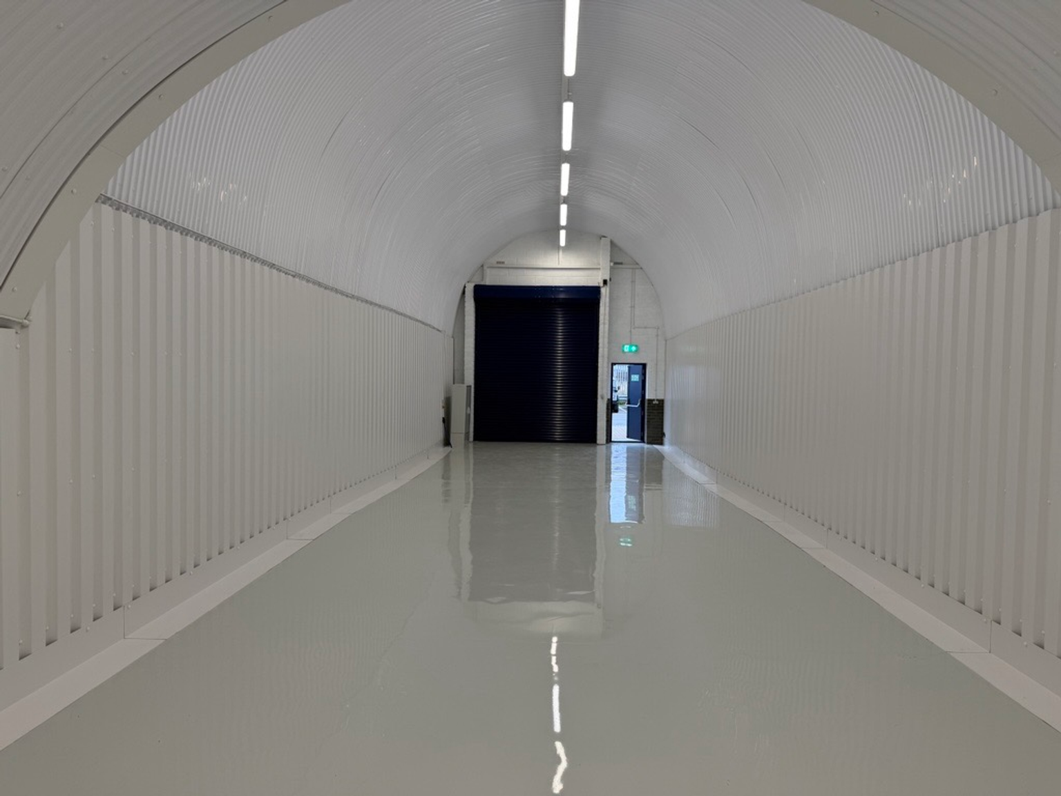 An empty arch with white lining, facing the front electric roller shutter entrance, which is open.