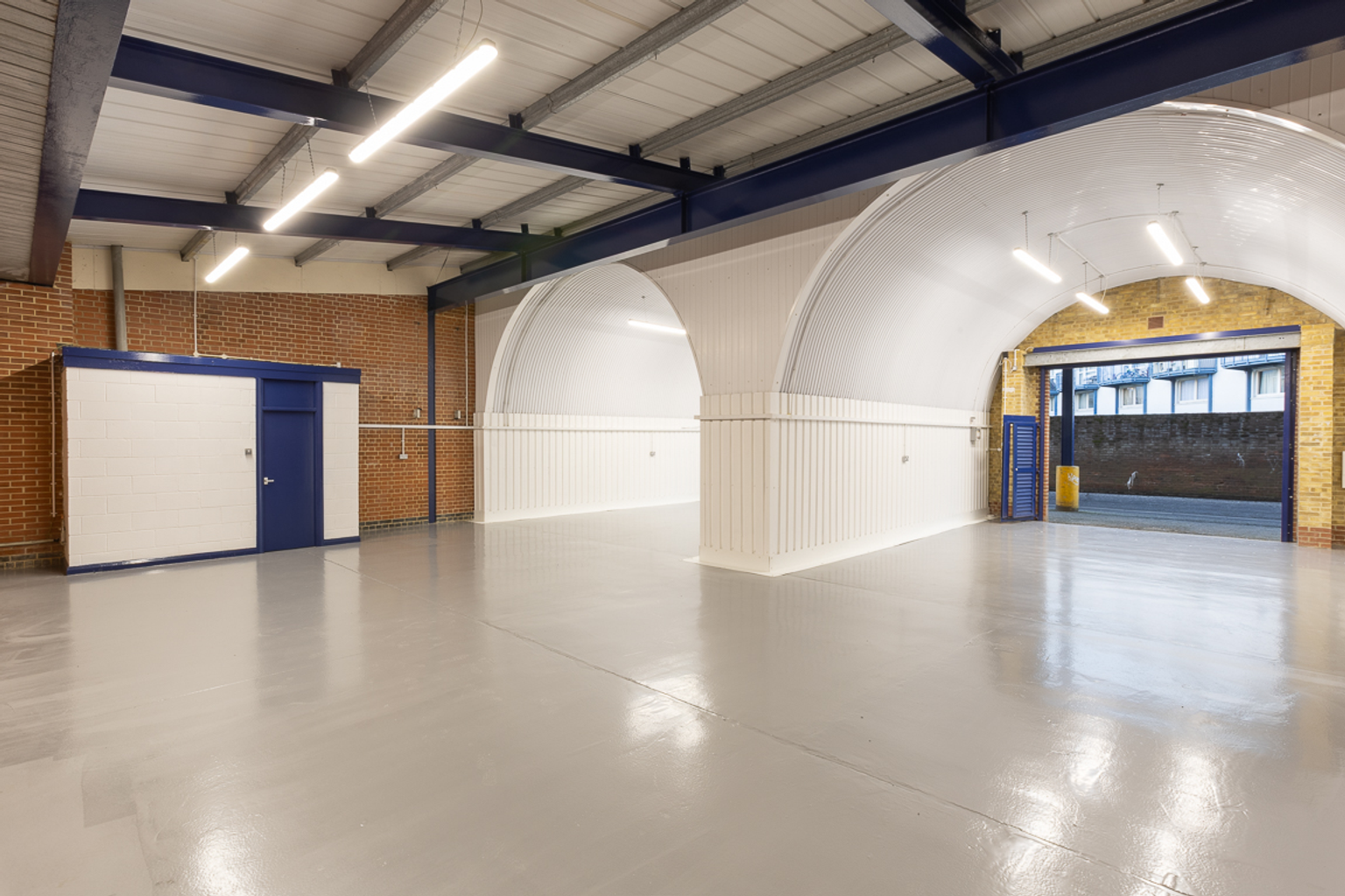 The interior of a warehouse unit, facing the front electric roller shutter, which is open and large enough for vehicle access.