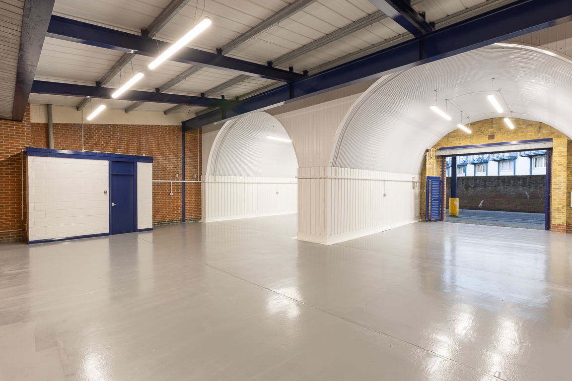 The interior of a warehouse unit, facing the front electric roller shutter, which is open and large enough for vehicle access.