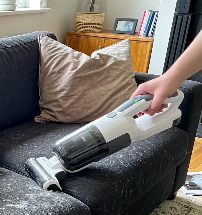 A person vacuuming pet hair off a couch with a handheld vacuum
